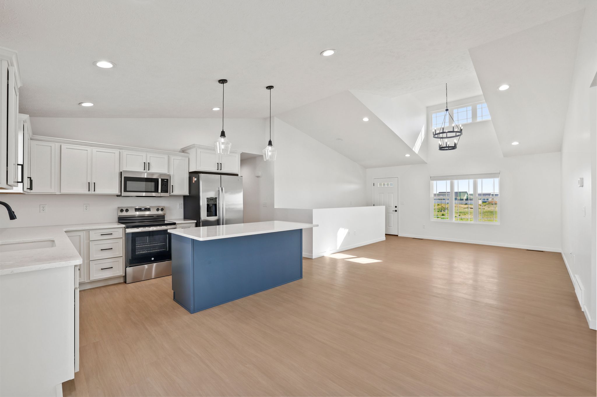 Open-concept kitchen and living space with white cabinets, a navy island, and vaulted ceilings